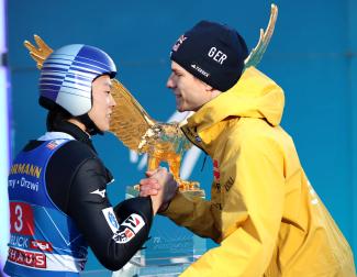 Fotomontage: Ryoyu Kobayashi und Andreas Wellinger geben sich die Hand, im Hintergrund die Trophäe für den Tourneesieger